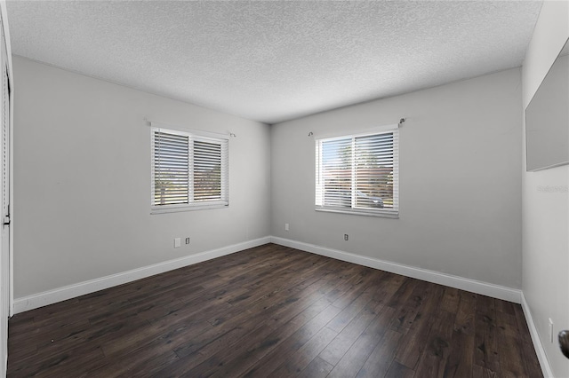 unfurnished room featuring dark wood-type flooring, a wealth of natural light, a textured ceiling, and baseboards