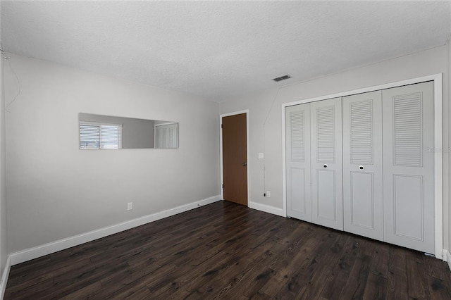 unfurnished bedroom with baseboards, visible vents, dark wood-style floors, a textured ceiling, and a closet