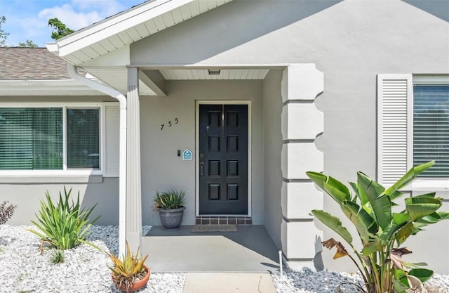 doorway to property featuring a shingled roof and stucco siding