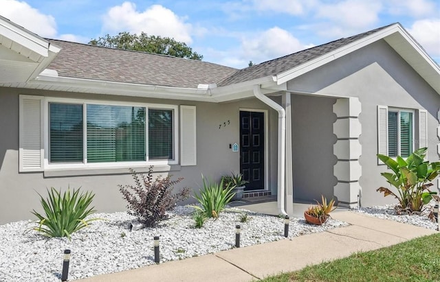 view of exterior entry with stucco siding and a shingled roof