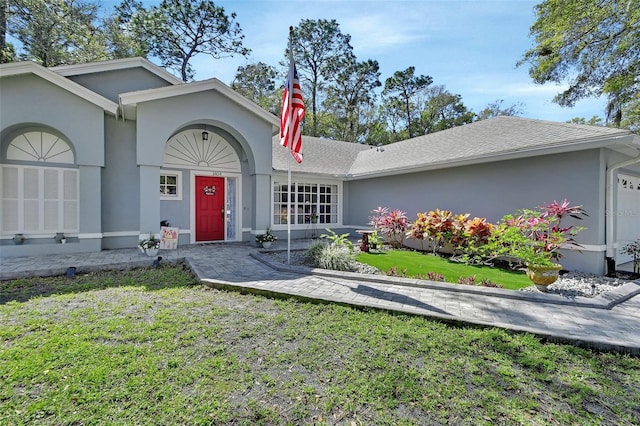 ranch-style home featuring a shingled roof, an attached garage, a front lawn, and stucco siding