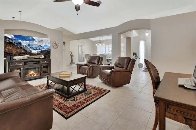 living room with arched walkways, a ceiling fan, a glass covered fireplace, vaulted ceiling, and light tile patterned flooring