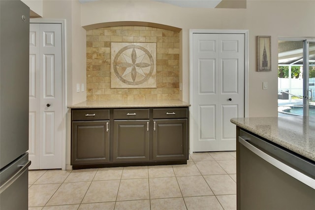 kitchen featuring backsplash, appliances with stainless steel finishes, light tile patterned flooring, dark brown cabinets, and light stone countertops