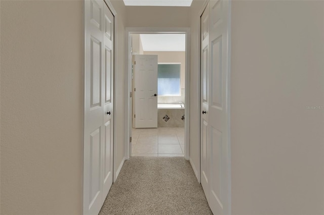 hall with light colored carpet, light tile patterned flooring, and a skylight