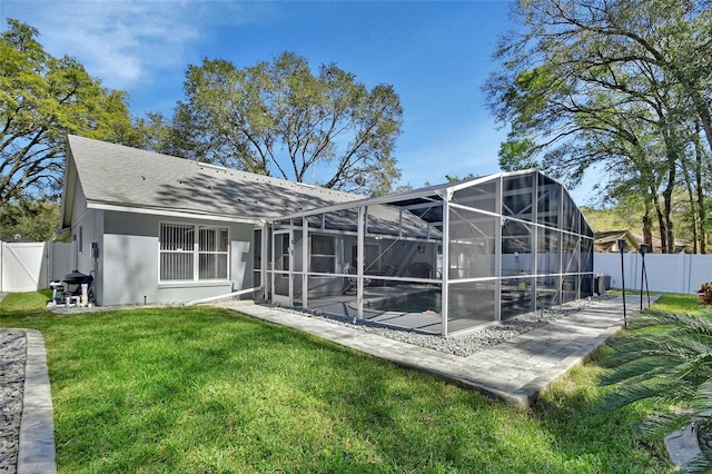 rear view of house with glass enclosure, a fenced backyard, a yard, a patio area, and stucco siding