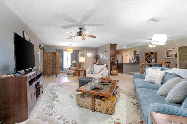 living area featuring a ceiling fan, visible vents, a textured ceiling, and light tile patterned floors