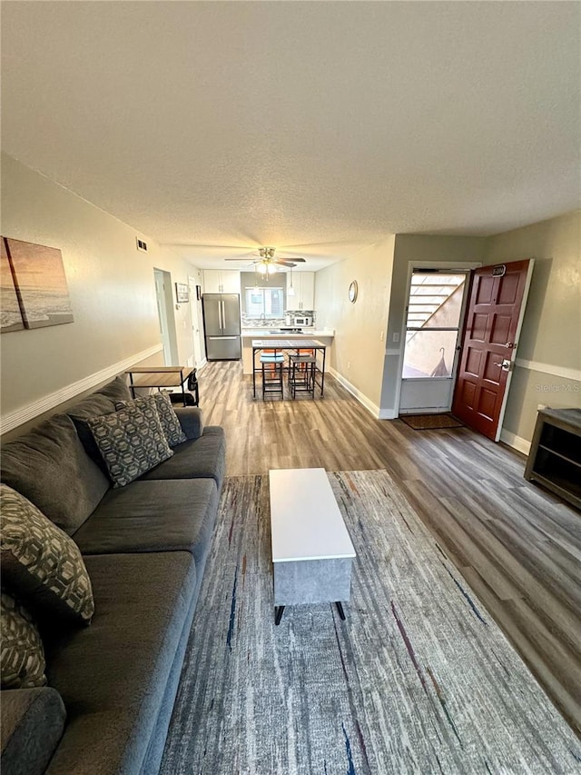 living area with a wealth of natural light, a ceiling fan, baseboards, and wood finished floors