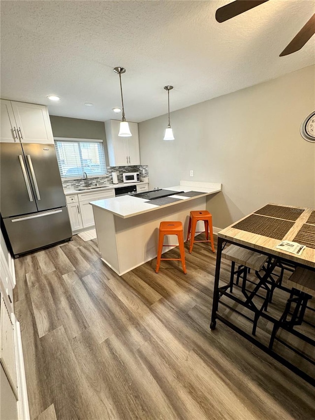 kitchen with white cabinets, a breakfast bar area, freestanding refrigerator, hanging light fixtures, and light countertops