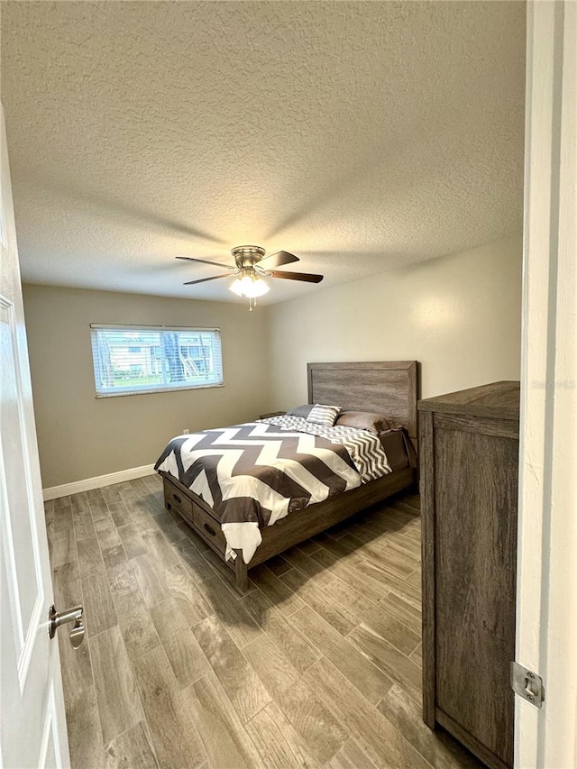 bedroom with a ceiling fan, a textured ceiling, baseboards, and wood finished floors