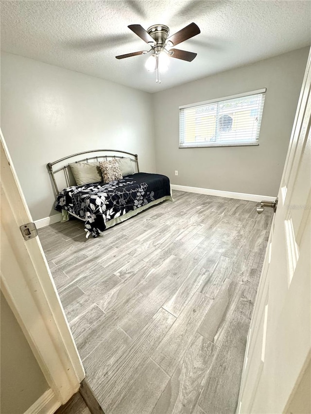 bedroom with a textured ceiling, wood finished floors, a ceiling fan, and baseboards