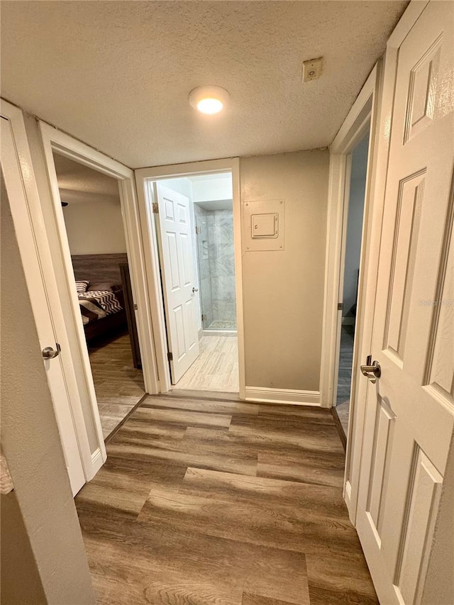 hallway with a textured ceiling, baseboards, and wood finished floors