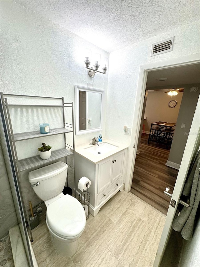 bathroom with a textured ceiling, a textured wall, toilet, vanity, and visible vents