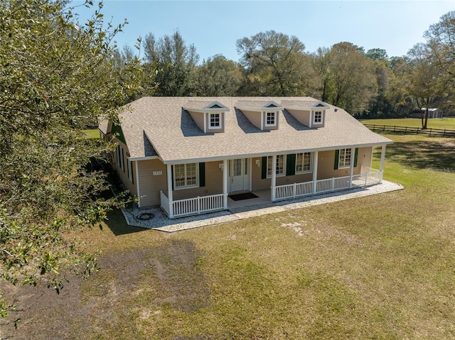 view of front of property featuring covered porch, a shingled roof, fence, and a front yard