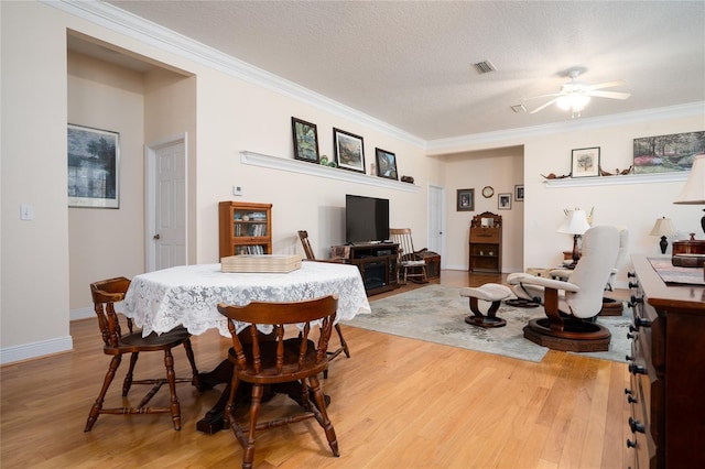 dining room with light wood-style floors, a textured ceiling, visible vents, and crown molding