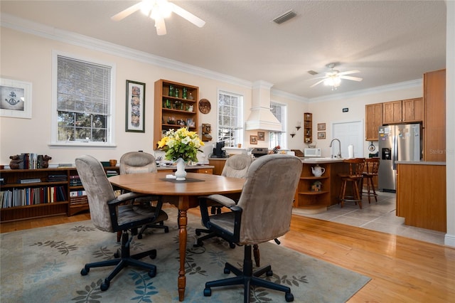 dining room with light wood finished floors, visible vents, ceiling fan, a textured ceiling, and crown molding