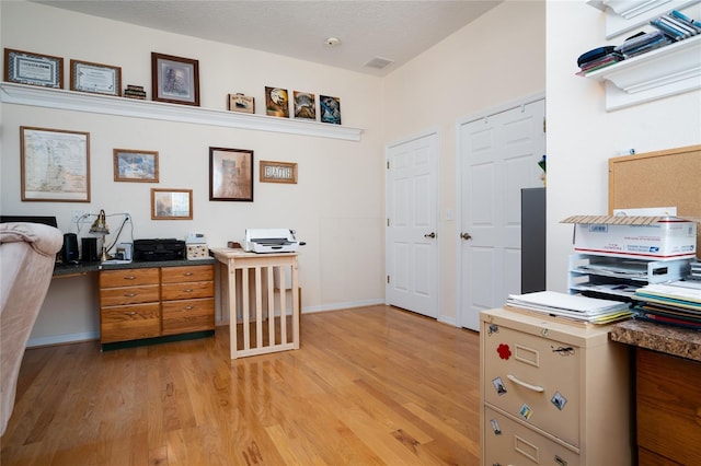 office area with a textured ceiling, light wood finished floors, visible vents, and baseboards