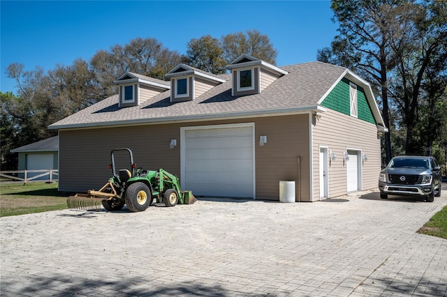 view of side of home with a garage, a shingled roof, fence, and decorative driveway