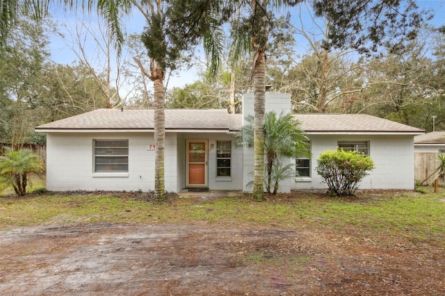 ranch-style house featuring roof with shingles, a chimney, concrete block siding, and fence