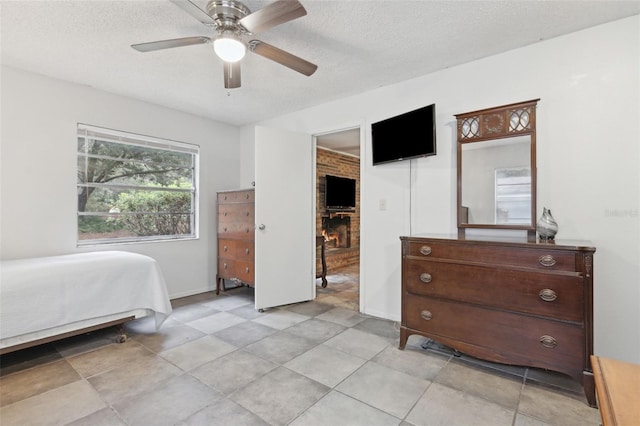 bedroom with a textured ceiling, ceiling fan, a brick fireplace, and baseboards