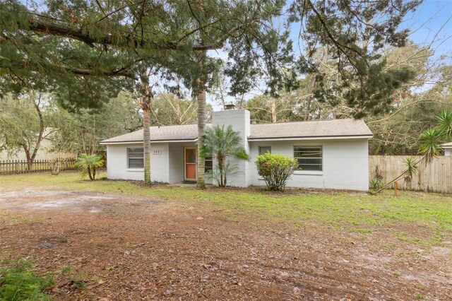 back of house featuring a chimney, concrete block siding, a lawn, and fence