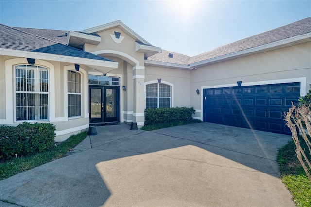 doorway to property with french doors, roof with shingles, concrete driveway, and stucco siding