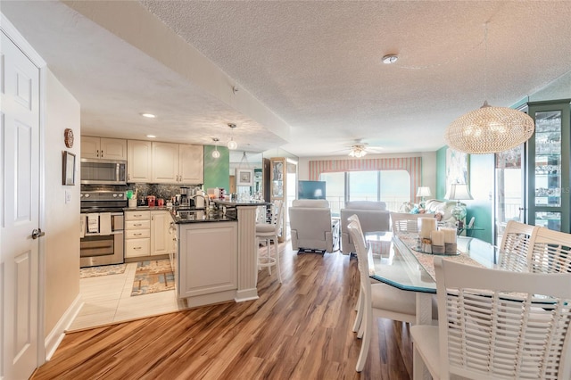 kitchen with a breakfast bar area, open floor plan, appliances with stainless steel finishes, light wood finished floors, and dark countertops