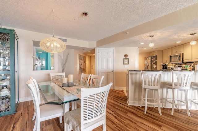 dining space featuring visible vents, baseboards, light wood-style flooring, and a textured ceiling