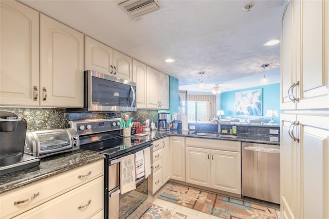 kitchen featuring visible vents, decorative backsplash, dark stone countertops, stainless steel appliances, and a sink