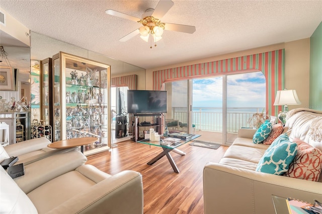 living area with a wealth of natural light, ceiling fan, a textured ceiling, and wood finished floors