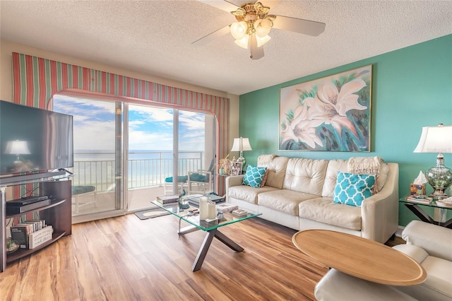 living room featuring a water view, a textured ceiling, a ceiling fan, and wood finished floors