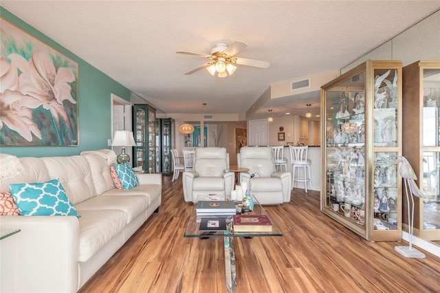 living area featuring a textured ceiling, ceiling fan, wood finished floors, and visible vents