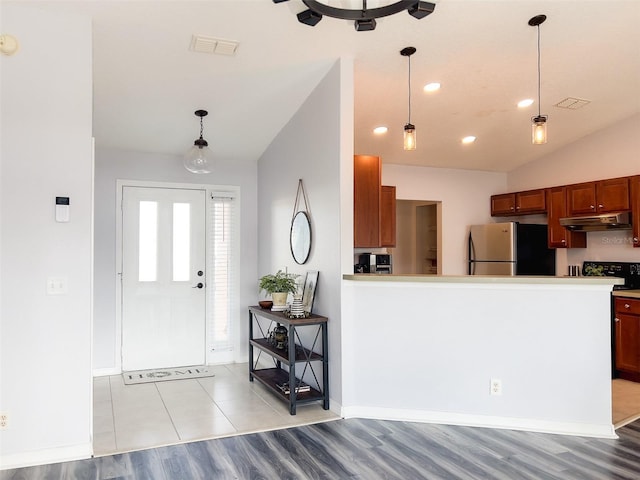 kitchen with hanging light fixtures, under cabinet range hood, visible vents, and freestanding refrigerator