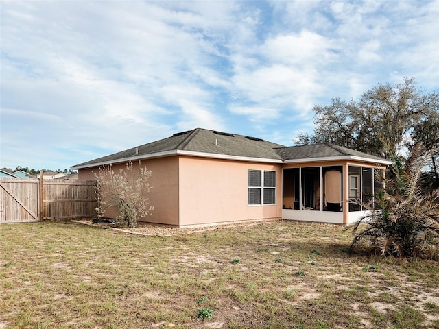 back of house with a sunroom, fence, a lawn, and stucco siding