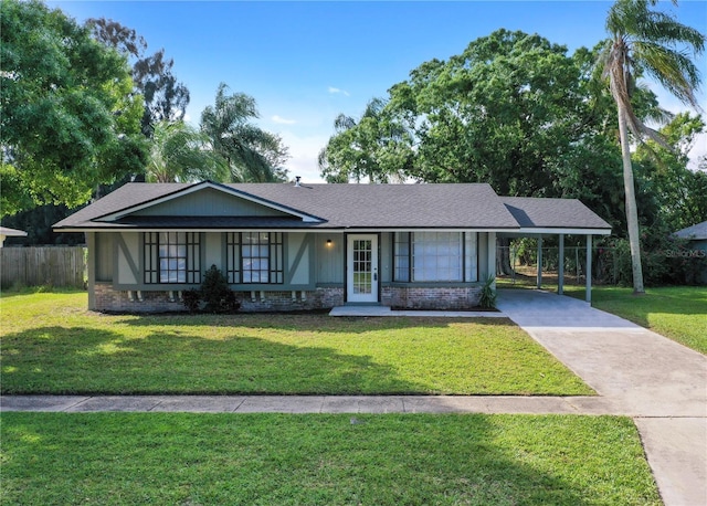 ranch-style house featuring driveway, a front lawn, a carport, and roof with shingles