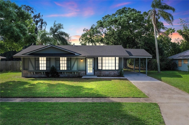 ranch-style house with driveway, a shingled roof, a front yard, a carport, and brick siding