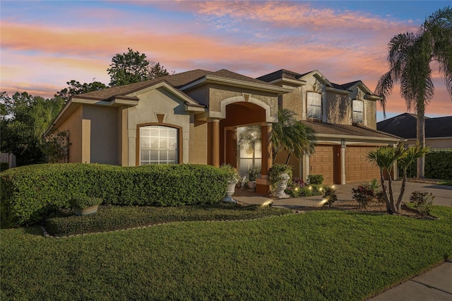 mediterranean / spanish home featuring stucco siding, driveway, a yard, and an attached garage