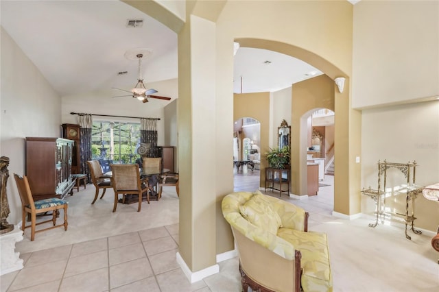 living area with high vaulted ceiling, a ceiling fan, arched walkways, light tile patterned floors, and light colored carpet