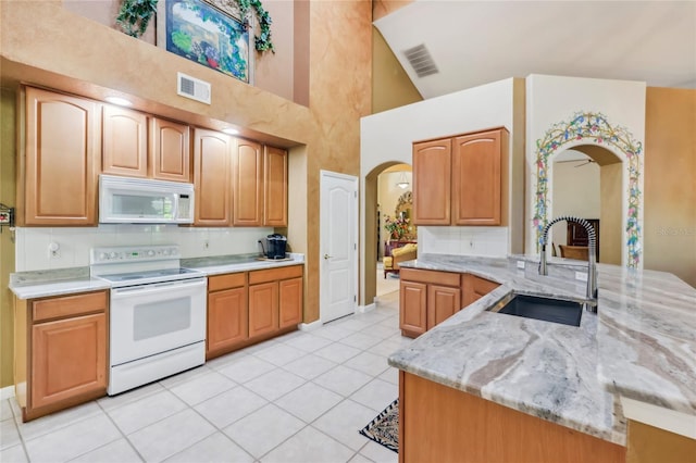 kitchen with visible vents, light stone countertops, arched walkways, white appliances, and a sink