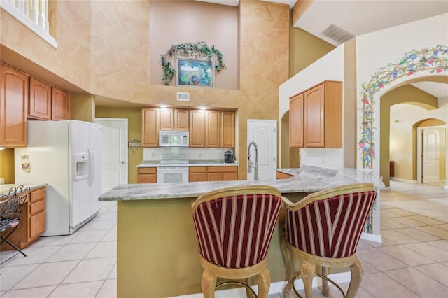 kitchen featuring white appliances, light tile patterned floors, visible vents, a peninsula, and a high ceiling