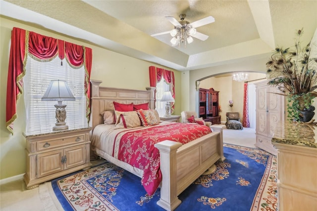 bedroom featuring a tray ceiling, carpet flooring, ceiling fan with notable chandelier, arched walkways, and a textured ceiling