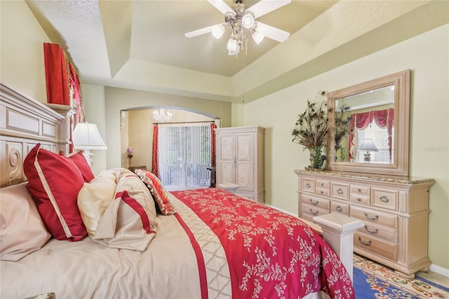 bedroom with ceiling fan, baseboards, a tray ceiling, arched walkways, and access to outside