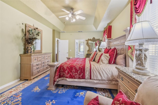 bedroom with a ceiling fan, a tray ceiling, baseboards, and visible vents