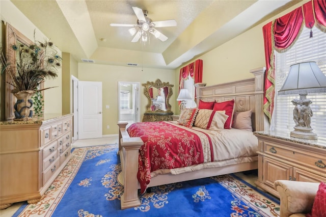 bedroom featuring a tray ceiling, a ceiling fan, visible vents, and baseboards