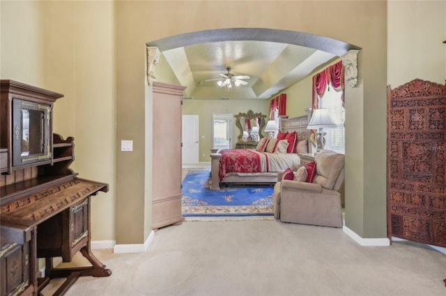 carpeted bedroom featuring a tray ceiling, baseboards, arched walkways, and ceiling fan