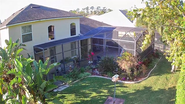 back of house with stucco siding, fence, a yard, roof with shingles, and a lanai