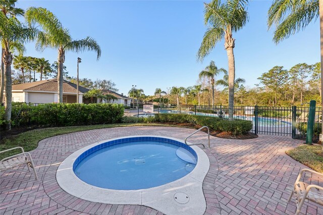 community pool with a patio area, a jacuzzi, and fence