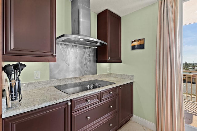 kitchen featuring light tile patterned floors, baseboards, wall chimney exhaust hood, light stone countertops, and black electric stovetop