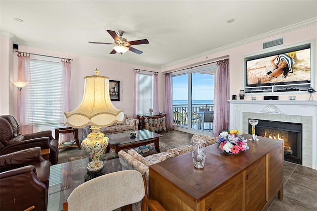 living area featuring a healthy amount of sunlight, visible vents, crown molding, and a tile fireplace