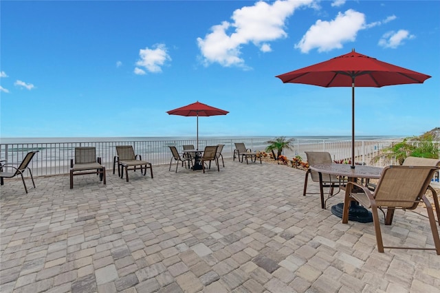 view of patio / terrace featuring a water view, fence, and a view of the beach