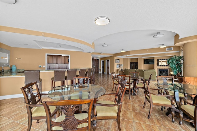 dining room featuring a glass covered fireplace, visible vents, vaulted ceiling, and baseboards